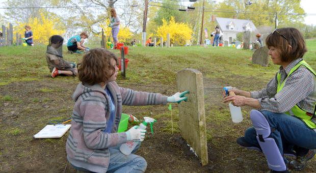 Jonathon Flaherty, a student at Cascade Brook School, discovered a potential error on a stone he was cleaning at Academy Corner Cemetery in Wilton. Deb Probert, right, a member of the Maine Old Cemetery Association, guided the stone-cleaning work.